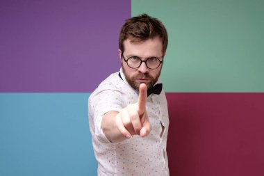 Yuvarlak gözlüklü sert adam işaret parmağıyla jest yapıyor, birini sakinleştirmeye çalışıyor ve kameraya sert bakıyor..