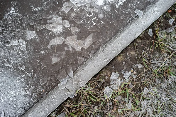 Frozen puddle with pieces of ice, dry lawn covered with hoarfrost and dividing their curb on a winter, cold day. — 스톡 사진