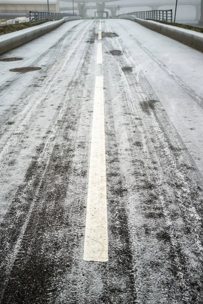 Camino de asfalto congelado con marcas, bordes y aceras, en el fondo del puente y viaducto, en un día de invierno frío y nublado . — Foto de Stock