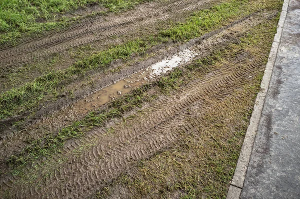 Stopy pneumatik na trávníku, část chodníku a hranice je oddělují. Poškození trávy v důsledku přepravy. Barbarský přístup k životnímu prostředí. — Stock fotografie