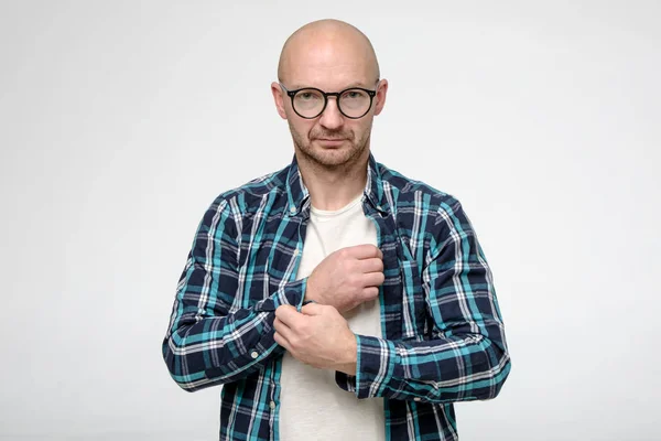 Hombre calvo serio, sin afeitar con gafas sujeta un botón en un puño de camisa y mira con confianza a la cámara . — Foto de Stock