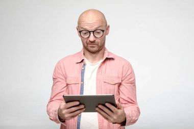 Gözlüklü kel adam, elinde tuttuğu tablete özenle bakıyor..