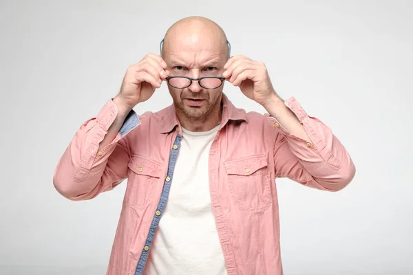 Enojado, hombre fruncido mira estrictamente a la cámara sobre las gafas que sostiene con las manos . — Foto de Stock