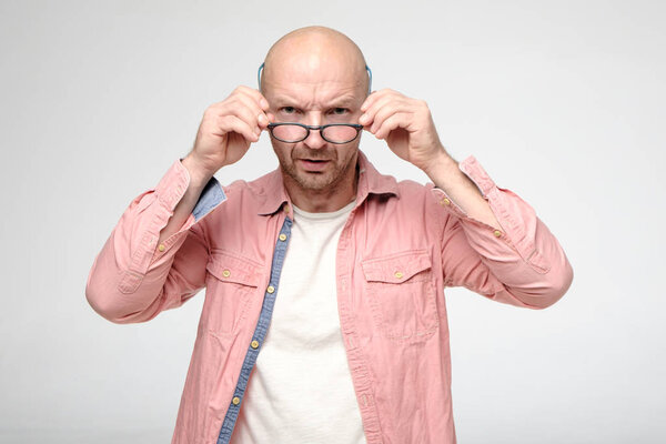 Злой, нахмуренный мужчина строго смотрит в камеру через очки, которые он держит руками.
.