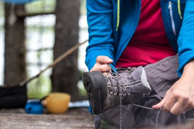 Kadın elleri, bulanık bir arka planda yürüyüş botlarını bağlar..
