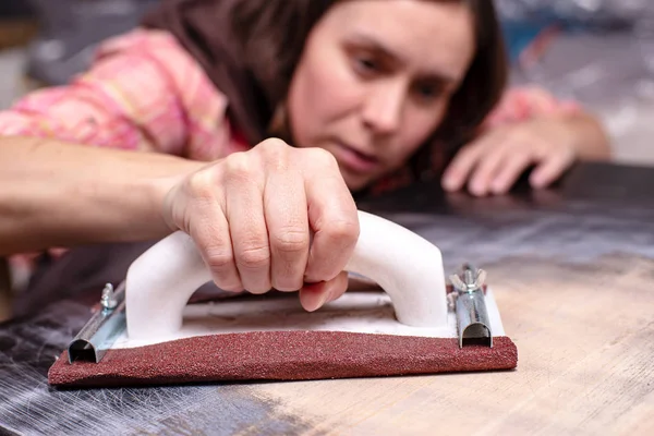 Kadın eli, zımpara kağıdı için bir marangoz tutacağı ile, eski ahşap yüzeyi siler ve parlatır, boyamaya hazırlanır.. — Stok fotoğraf