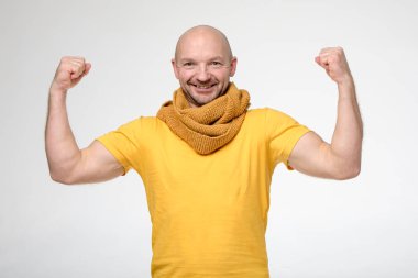 Parlak sarı tişörtlü ve atkılı güçlü, pozitif adam kollarını büktü ve kaslarını gösterdi, gülümsedi ve kameraya baktı..