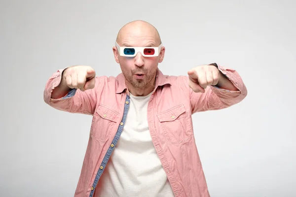 Excited, surprised bald man watches a movie in 3D glasses, he emotionally stood up and points a finger at the screen. — 스톡 사진