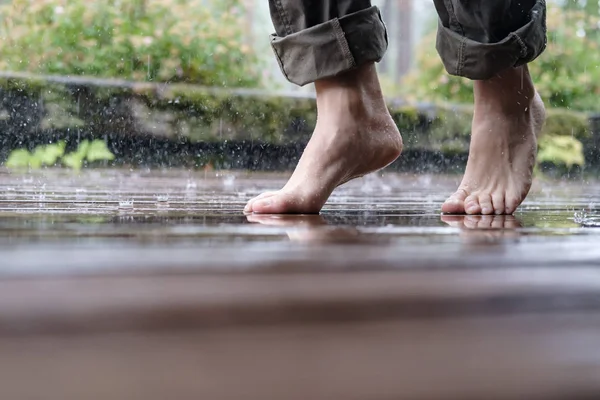 Ξυπόλητη γυναικεία πόδια περπατούν στο ξύλινο πάτωμα της αυλής, στη βροχή του καλοκαιριού, σε ένα θολό φόντο. — Φωτογραφία Αρχείου