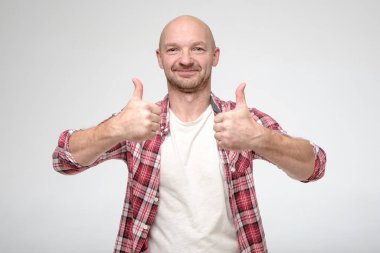Tatmin olmuş beyaz bir adam, elleri ve başparmaklarıyla onaylayıcı bir jest yapar, gülümser ve kameraya bakar..