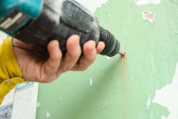 Reparación. Las manos masculinas usando un taladro perforador eléctrico con un taladro hacen un agujero en la pared con pintura pelada . —  Fotos de Stock