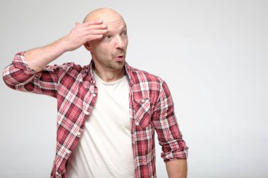 Komik, şoke olmuş kel bir adam, yüzünde tuhaf bir ifadeyle, başının yakınında el ele tutuşuyor ve yan tarafından şaşırmış görünüyor. Boşluğu kopyala.