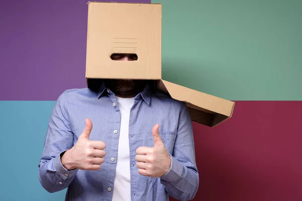 Funny, weird man put a cardboard box on head and shows a positive gesture, thumbs up. Concept of shelter from problems.