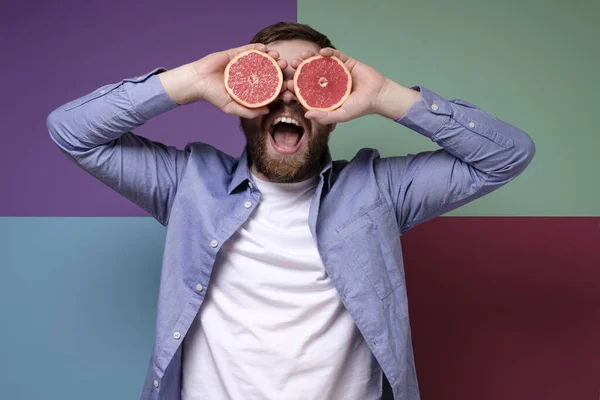 Radostný vousatý muž se dvěma půlkami jasného šťavnatého grapefruitu místo očí se usměje a baví se. Čerstvý pohled. Tvůrčí nápad. — Stock fotografie