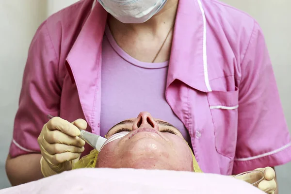 Cosmetologist usa uma escova para aplicar uma máscara calmante, transparente e branca na pele avermelhada do rosto dos pacientes, após o descascamento químico . — Fotografia de Stock