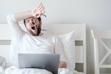 Adam gözlüğünü çıkardı ve esnedi. Yeterince uyuyamadı. Sabahın erken saatlerinde yumuşak bir yatakta dizüstü bilgisayarla çalışıyor..