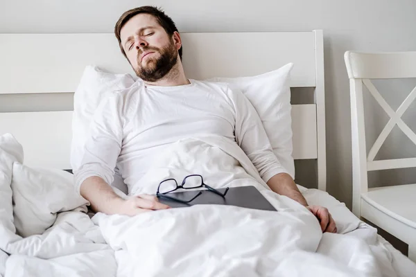 Bearded man fell asleep sitting in bed, in the early morning, he worked with a laptop all night and was very tired. — Stock Photo, Image