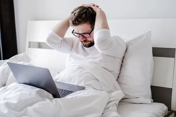 Mannen i pyjamas är upprörd, han arbetade hela natten med en laptop i sängen och avslutade inte projektet. — Stockfoto