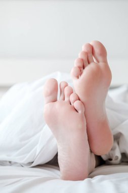 Beyaz bir battaniyenin altında, yatakta, rahat bir dairede, doğal ışıkta, fotokopi alanı ile. Dikey fotoğraf.