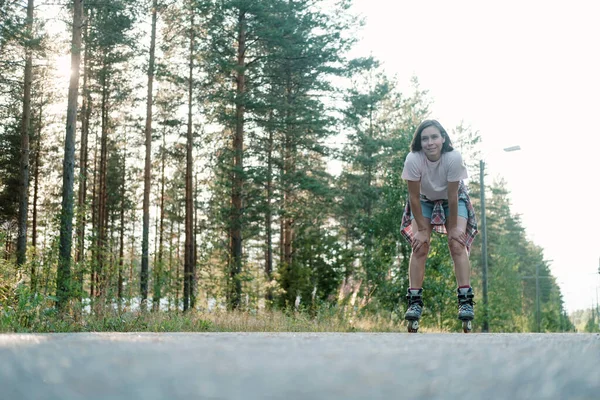 Leende kvinna på rullskridskor vilar efter ridning i hög hastighet på vägen, på en sommardag. Bottenvy. Aktiv semester. — Stockfoto