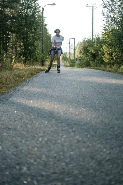 Tevreden, lachende vrouw rolschaatst op hoge snelheid op een zomerse dag tussen de bomen door. Actieve vakanties. — Stockfoto