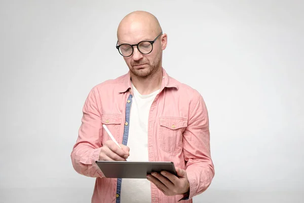 Seriös, fokuserad person med glasögon, arbetar med en tablett och stylus. — Stockfoto