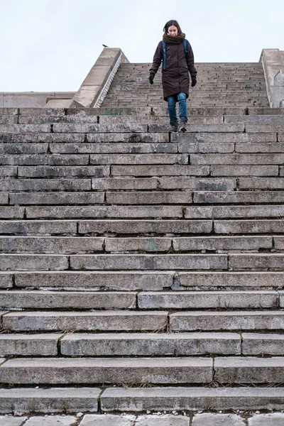 Ικανοποιημένος τουρίστας με ζεστά ρούχα και με σακίδιο πόλης κατεβαίνει τα παλιά πέτρινα σκαλοπάτια μιας επικίνδυνης σκάλας. Κάτω όψη. — Φωτογραφία Αρχείου