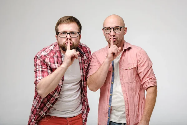 Two men say silence, making a gesture with an index finger on their lips and look excitedly at the camera. Secret of friends. Shh. — Stock Photo, Image