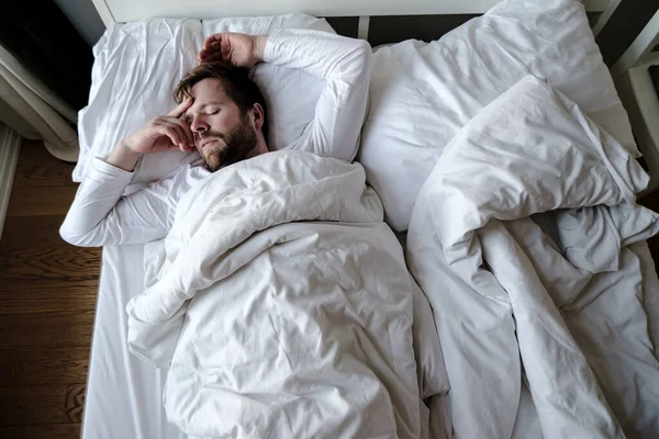 Hombre barbudo duerme inquieto en la cama, él está alarmado y tuvo una pesadilla terrible . — Foto de Stock