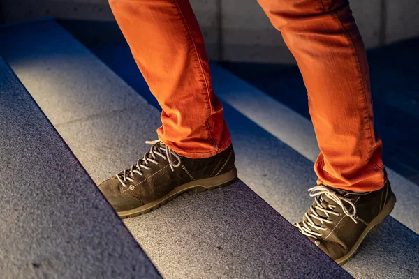 Las piernas masculinas con botas y pantalones vaqueros rojos suben los escalones de piedra iluminados en una noche de invierno. Primer plano . — Foto de Stock