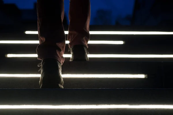 Las patas masculinas en botas suben los escalones de piedra iluminados en una noche de invierno. Vista inferior . — Foto de Stock