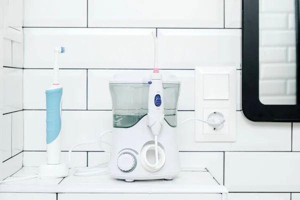 Electric oral irrigator and a rechargeable toothbrush are in the white tiled bathroom, next to the mirror. — Stock Photo, Image