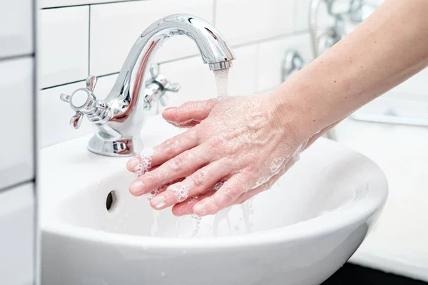Lavarse las manos con espuma jabonosa, bajo agua corriente, en el baño . — Foto de Stock