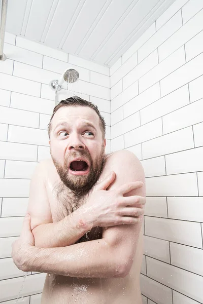 Homem com uma expressão estúpida em seu rosto se sente chocado em tomar um banho frio, ele congelou e grita, cobrindo seu corpo com as mãos — Fotografia de Stock