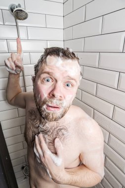 Man in soapy foam was upset because the water in the shower was over and with unhappy eyes looked into the camera.
