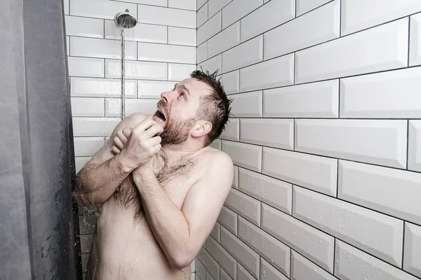 Hombre sorprendido mira una regadera en el cuarto de baño, de la que, inesperadamente, el agua fría está vertiendo . — Foto de Stock