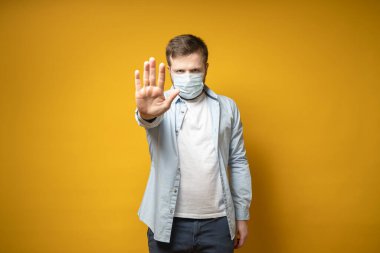Serious man in a medical mask on his face makes a stop gesture with his hand, protecting against the virus. Health concept.