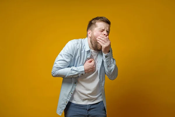 Der Mann hustet, bedeckt den Mund mit der Handfläche und hält die Hand auf die Brust, wobei er Schmerzen verspürt. Konzept der Ausbreitung des Virus. — Stockfoto