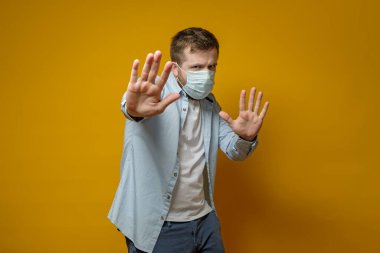 Man with a medical mask on face makes a stop gesture with hand and tries to protect himself from the virus. Health concept. clipart