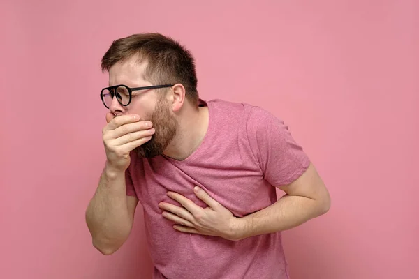 Mann mit Brille, hustet, bedeckt Mund mit Handfläche und hält Hand auf Brust und empfindet Schmerzen. Konzept der Ausbreitung des Virus. — Stockfoto