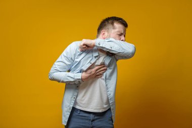 Man coughs in his elbow and holds hand on chest, experiencing pain. Correct sneezing. Concept of spread of the virus.