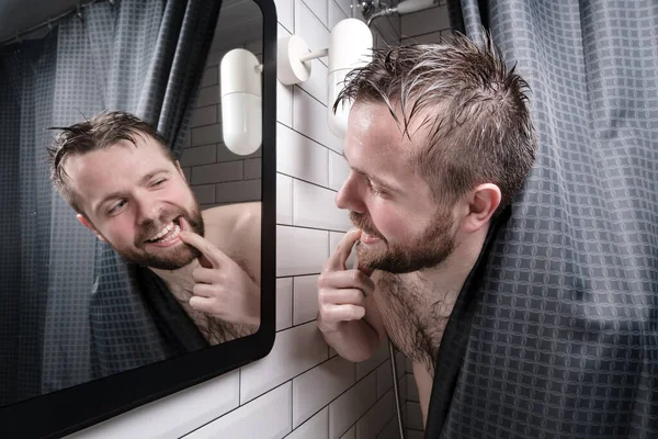 Contented man carefully examined his beautiful, healthy teeth in the mirror, peering out from behind the curtains in shower. — Stock fotografie