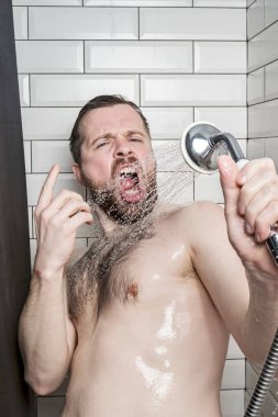 Funny bearded man sings in the bathroom, using a shower head with running water instead of a microphone. Lifestyle.