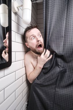Frightened man peeks out from behind the curtains, in the shower, he is shocked, opened mouth and makes big eyes.