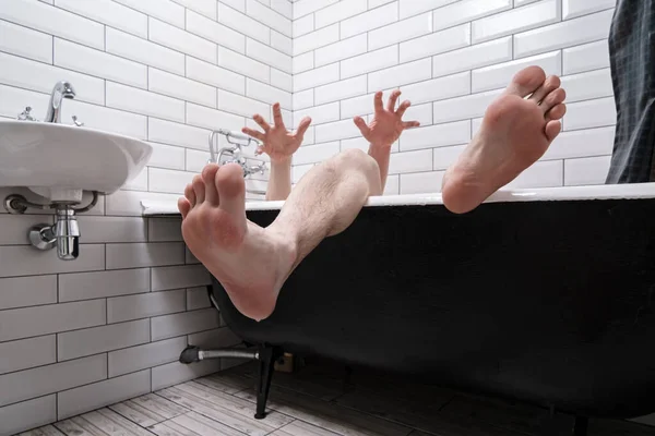Las piernas y manos húmedas masculinas con los dedos extendidos son visibles desde la bañera de hierro fundido en el interior del baño moderno . — Foto de Stock