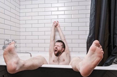 Man relaxedly sits in a cast-iron bath with legs hanging out, yawns and stretches, after water procedures. Lifestyle.