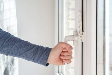Female hand closed a modern white PVC window, with an attached fixing device for ventilation, in natural light.
