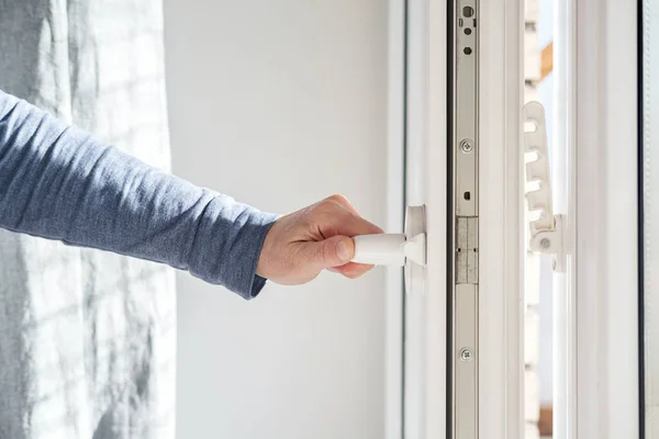 Hand opens a PVC window, holding the handle in a horizontal position, with a fixing device attached to the frame for ventilation. — 스톡 사진