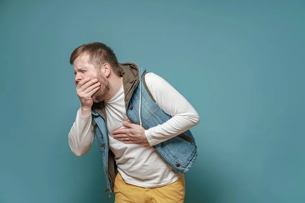 Mann in Jeansweste hustet in Handfläche und hält Hand auf Brust und empfindet Schmerzen. Konzept der Ausbreitung des Virus. — Stockfoto