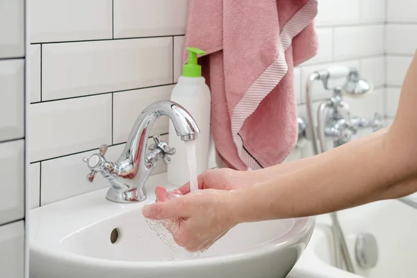 Lavarse las manos bajo el agua corriente para protegerse contra un virus peligroso, jabón líquido y una toalla están cerca. Concepto de salud . — Foto de Stock